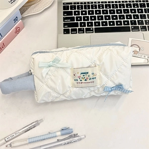 Close-up of quilted glossy white pencil case with blue zipper and decorative bows