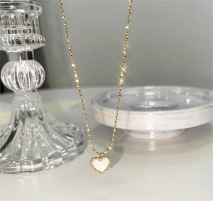 Detailed close-up of golden heart pendant with white shell inlay on a shimmering chain