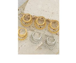 Detail shot of 18K gold and silver C-shaped twisted rope earrings on beige stone