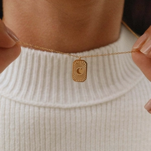 Detail of 18K gold-plated star and moon pendant necklace on a white sweater