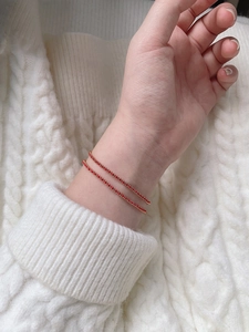 Detail of red beaded hand-woven bracelet with gold-plated stainless steel charms on a model