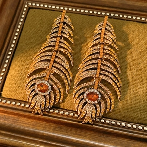Detailed macro of vintage gold feather earrings with orange rhinestones on green velvet
