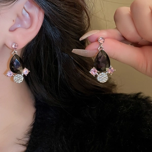Detailed close-up of teardrop earrings with black stones and pink crystals on model