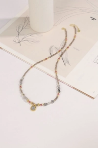 Macro shot of beaded necklace with smoky crystal, pink accents and gold square pendant