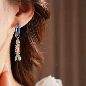 Close-up of model wearing cartoon fishbone enamel drop earrings in blue and white