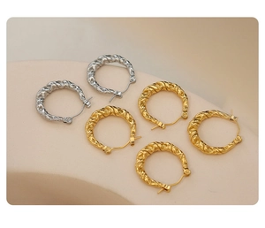 Detailed view of twisted gold and silver hoop earrings on a minimalist beige background