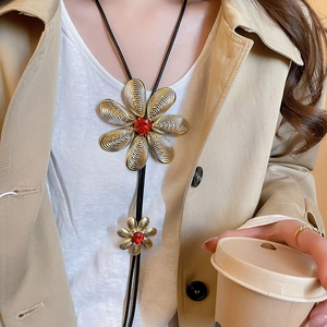 Detail of flower necklace with red gemstone pendant worn on trench coat and white shirt