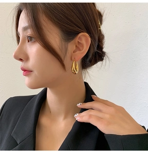 Close-up of golden teardrop earrings on a model showing smooth mirror finish