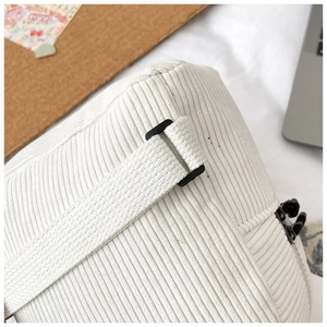 Detail view of white corduroy backpack strap with sturdy black buckle and neat stitching