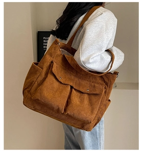 Brown corduroy tote bag showing large capacity and front pockets worn on the shoulder