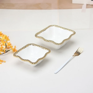 Macro shot of white square ceramic sauce bowls with gold beaded edge and gold fork