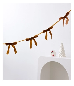 Caramel velvet bow banner hanging on a white wall with festive Christmas decorations