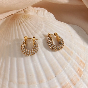 Detail of 18K gold-plated U-shaped earrings with cubic zirconia on a white shell