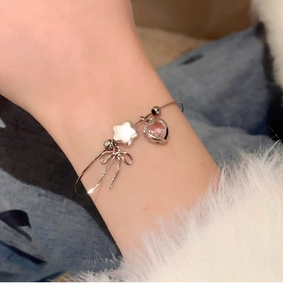 Detail of silver bow and pink heart charms on a sleek open bracelet for women