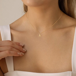 Close-up of a minimalist gold initial A pendant necklace worn on a woman's collarbone