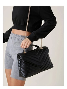 Black V-quilted faux leather crossbody bag with gold chain strap shown on a model