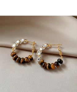 Close-up of golden C-shaped hoop earrings with tiger eye and zircon on champagne silk