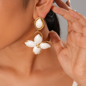 Close-up of golden oval hollow flower earrings with white gemstones worn by a model