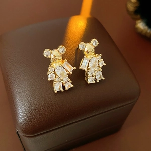Macro shot of gold plated bear earrings with sparkling zircons on brown leather texture