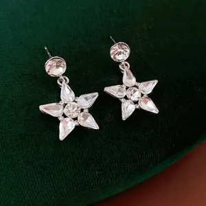 Silver star pendant earrings with crystal rhinestones on dark green velvet background