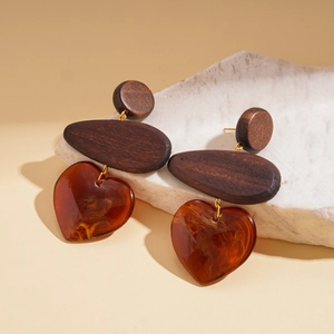 Detail of bohemian wood and amber resin heart earrings on white stone display
