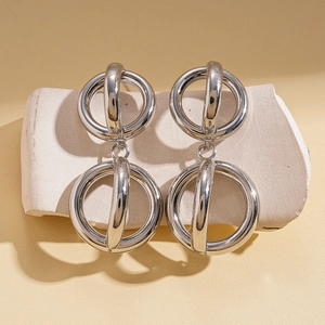 Close-up of geometric hollow silver double circle earrings on a beige stone base