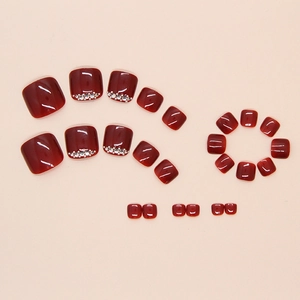 Detail of wine red press-on toenails with glossy finish and sparkling silver rhinestones