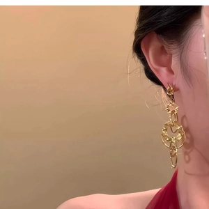Detail of long gold geometric hollow circle drop earring worn by a model on a warm background