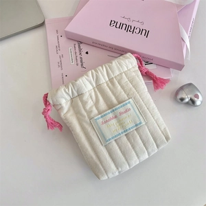 Detailed view of quilted makeup pouch with pink drawstring and soft cream fabric texture