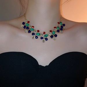 Luxurious gold necklace featuring green and blue teardrop gems worn by a model