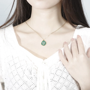 Detail showing a golden Taurus zodiac pendant with green malachite texture on a model