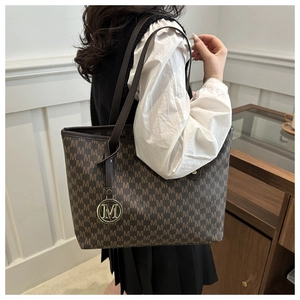 Détail d'un grand sac cabas marron à motif M et pendentif doré porté par un mannequin