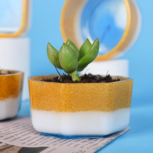 Dettaglio di un vaso esagonale in resina con glitter dorati e design bicolore bianco