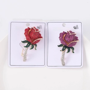 Dettaglio di spille a rosa rosse e viola con cristalli scintillanti su carta bianca