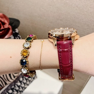 Close-up of vintage bronze bracelet with colorful gemstones and red leather strap watch