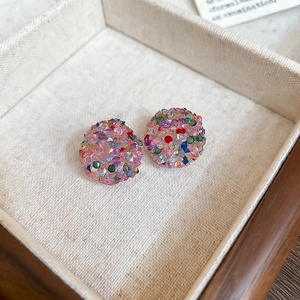 Close-up of colorful rhinestone-encrusted sphere stud earrings in a cream jewelry box