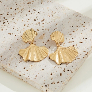 Detailed view of gold ginkgo leaf earrings with metallic texture on a stone base