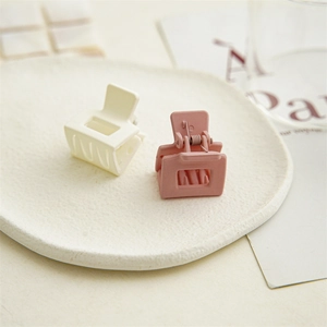 Close-up of matte square hair claws in beige and pink on a white textured plate
