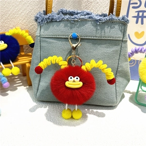 Cute red plush monster keychain with yellow spring tentacles on a blue denim bag