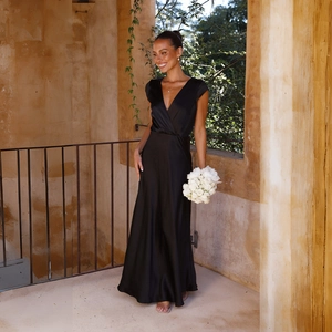 Elegant black satin V-neck mermaid maxi dress showcased in a sunlit stone arcade