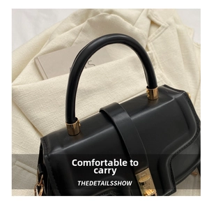 Close-up of black leather saddle bag featuring round handle and gold metal lock hardware
