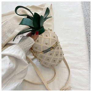 Detail of cream pineapple crossbody bag with gold studs and green leaf top handle