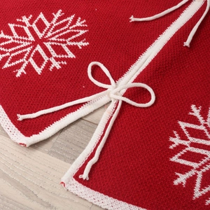 Red Christmas tree skirt with white snowflake patterns and knitted texture on wood floor