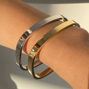 Close-up of sleek gold and silver stainless steel flat bangles worn on a model's wrist