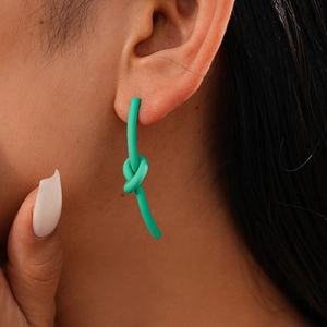 Dettaglio di un orecchino creativo verde menta a forma di nodo indossato da una modella