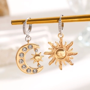 Détail de boucles d'oreilles dorées asymétriques avec lune, soleil et strass brillants