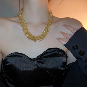 Detail of a chunky gold-tone woven collar necklace displayed on a female model neck