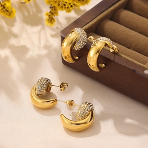 Golden C-shaped earrings with inlaid crystals on a wooden jewelry box