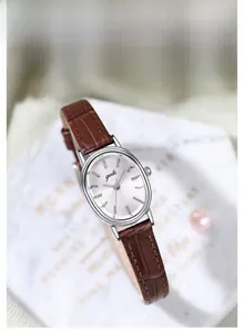 Close-up of oval silver watch with brown leather strap and sunray dial detail