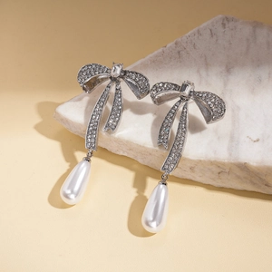 Détail de boucles d'oreilles nœud argentées avec strass et pendentif en perle d'eau